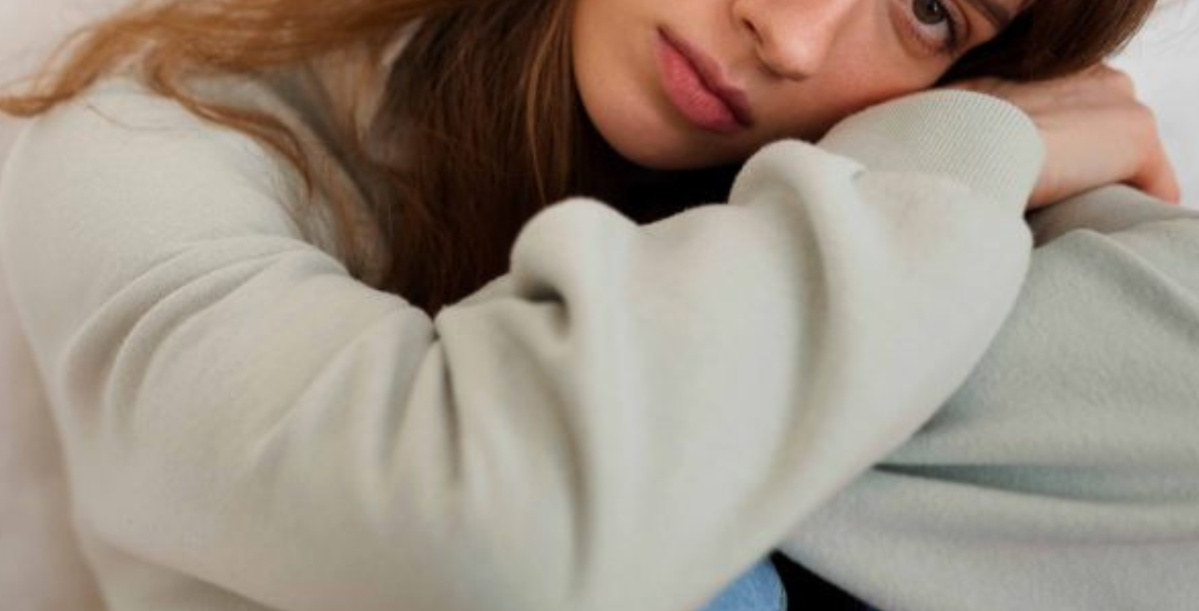 menina com ar de tristeza, com a cabeça apoiada nos braços cruzados sobre as pernas encolhidas