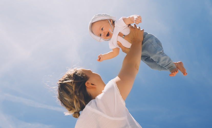 mãe a pegar no seu bebé ao colo com céu azul como fundo